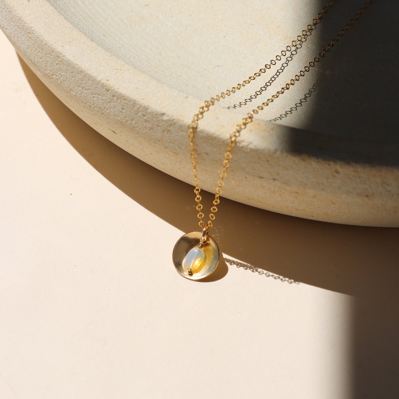 14k gold fill delicate chain necklace with opal charm and circle domed charm on a light dish