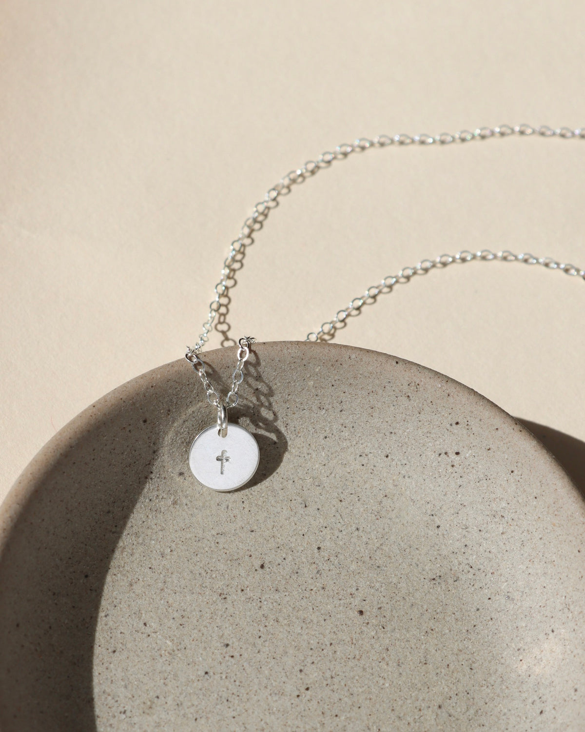Sterling silver delicate chain necklace with a sterling silver hand stamped cross charm in the sunlight