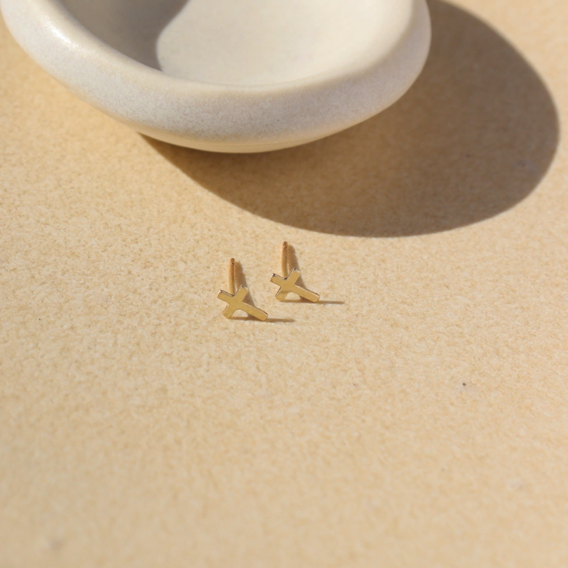 14k gold fill cross shaped studs on a light dish
