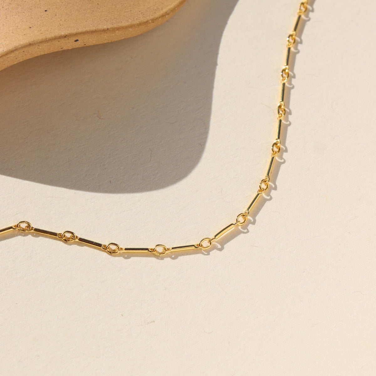 Bar and Link 14k gold fill chain close up laid on a beige background in the sunlight 