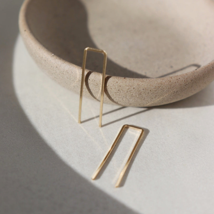 14k gold fill Staple earrings placed in the sunlight on a gray plate. A minimal earring that's perfect for everyday. Wear them in your second ear holes or let them be the main adornment for your ear lobes! Either way, these earrings will become one of your daily staples (pun, intended!).