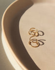 14k gold fill Mini Twist Earrings laid on a peach colored plate in the sunlight. These earring have a little twist giving the allusion that you have two piercings.