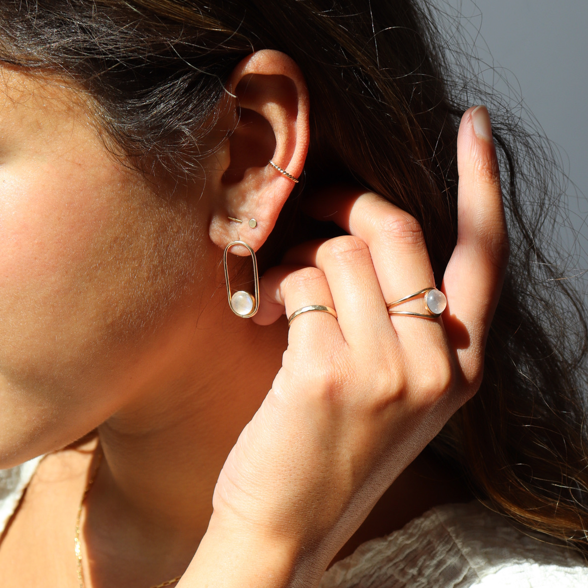 A post earring with 14k gold fill wire earring with a 8mm moonstone gemstone. The earrings are worn by a model, who is also wearing other 14k gold fill and moonstone jewelry. Her hand is up tucking her hair behind her ear.