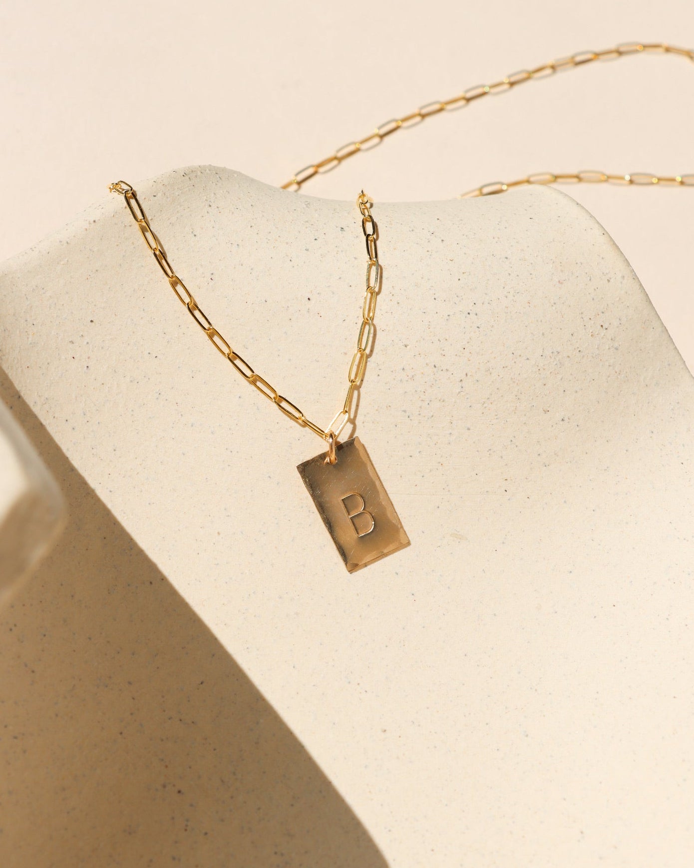 14k gold fill hand stamped pendant on a paperclip chain necklace on a light dish