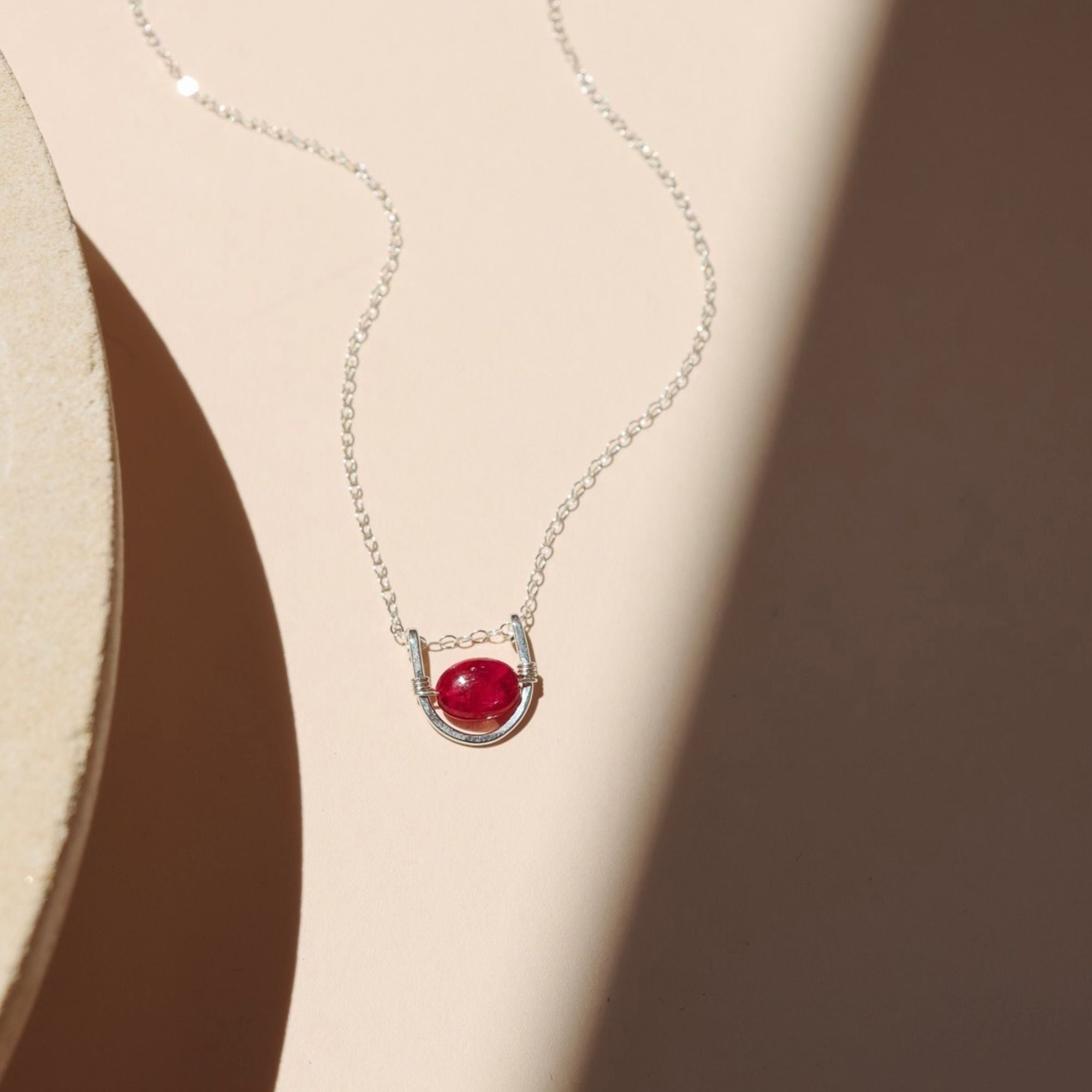 sterling silver chain necklace with ruby and wire pendant on a light surface