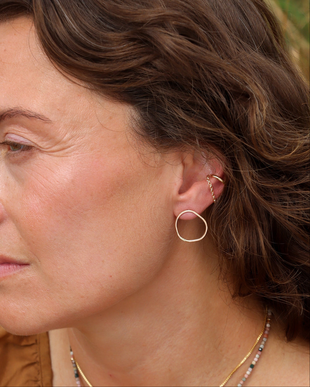 Woman wearing a hammered gold hoop earring with layered gold ear cuffs and delicate chain details.