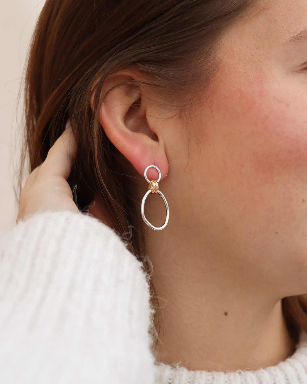 Close-up of a model wearing Token Jewelry's mixed metal Forma Earrings, featuring sterling silver circular and oval links connected by gold fill accents for a modern two-tone drop earring design.