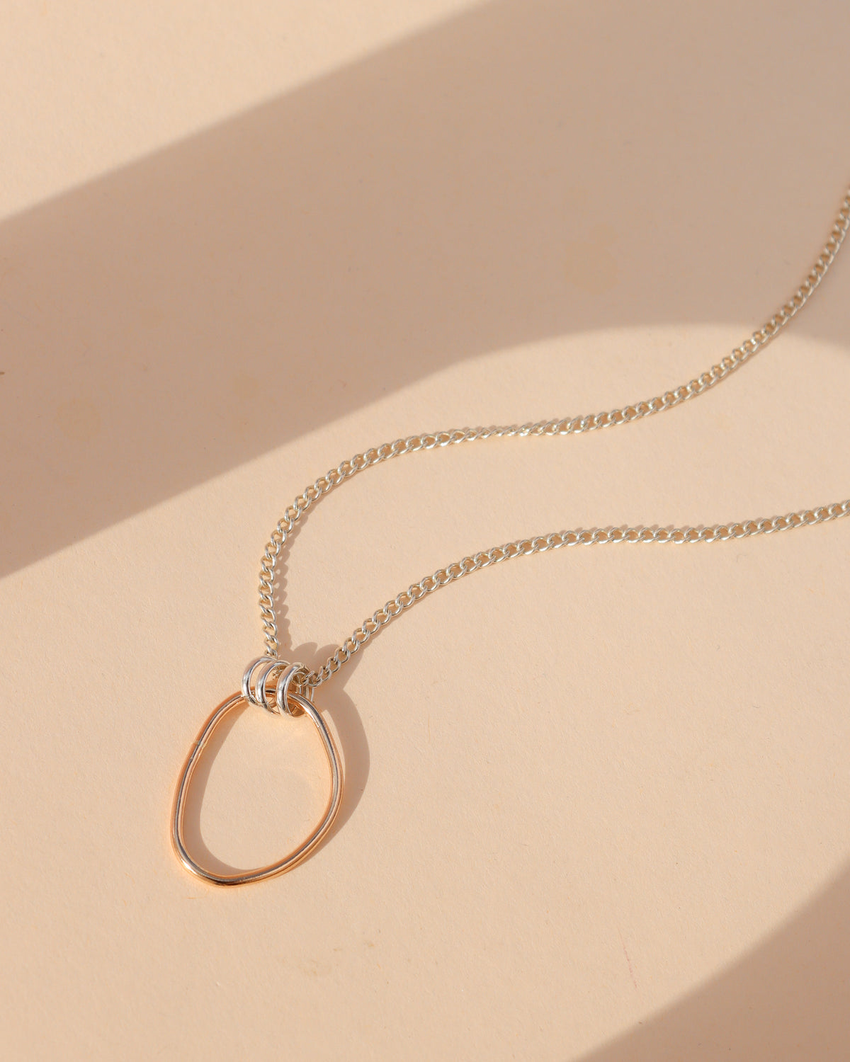Forma mixed metal pendant necklace featuring an organic, open oval gold fill pendant connected by sterling silver rings to a sterling silver chain, photographed in sunlight.