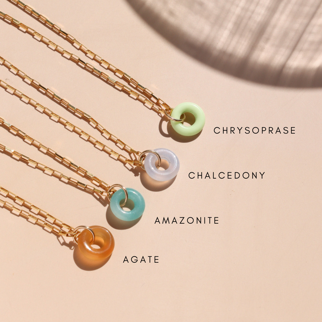row of 14k gold fill chain necklaces with agate, amazonite, chalcedony, and chrysoprase donut charms on a light surface