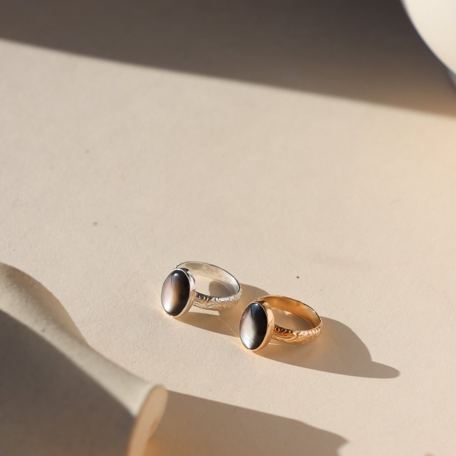 Moonflower rings in gold and silver with oval luminous stones, styled on a neutral surface in soft natural light.