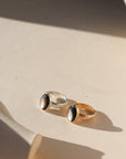 Moonflower rings in gold and silver with oval luminous stones, styled on a neutral surface in soft natural light.