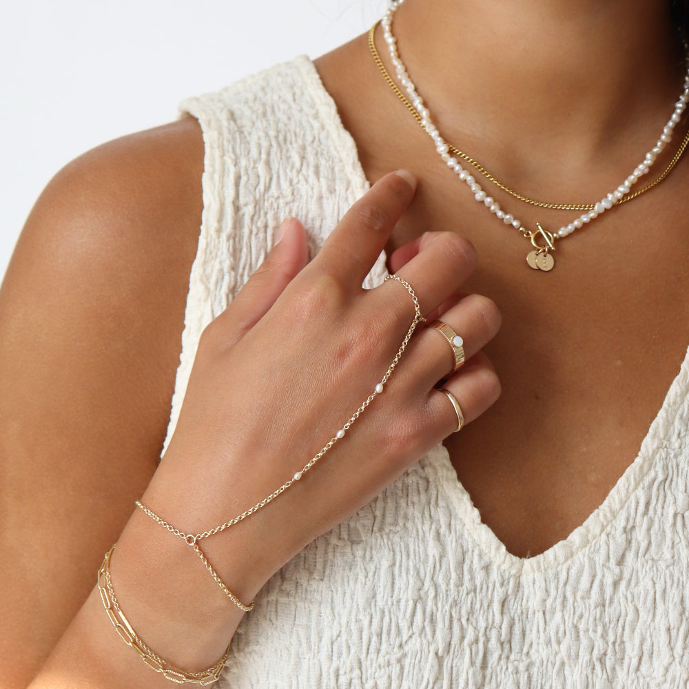 Model wearing 14k gold fill hand chain with pearls paired with other 14k gold fill jewelry