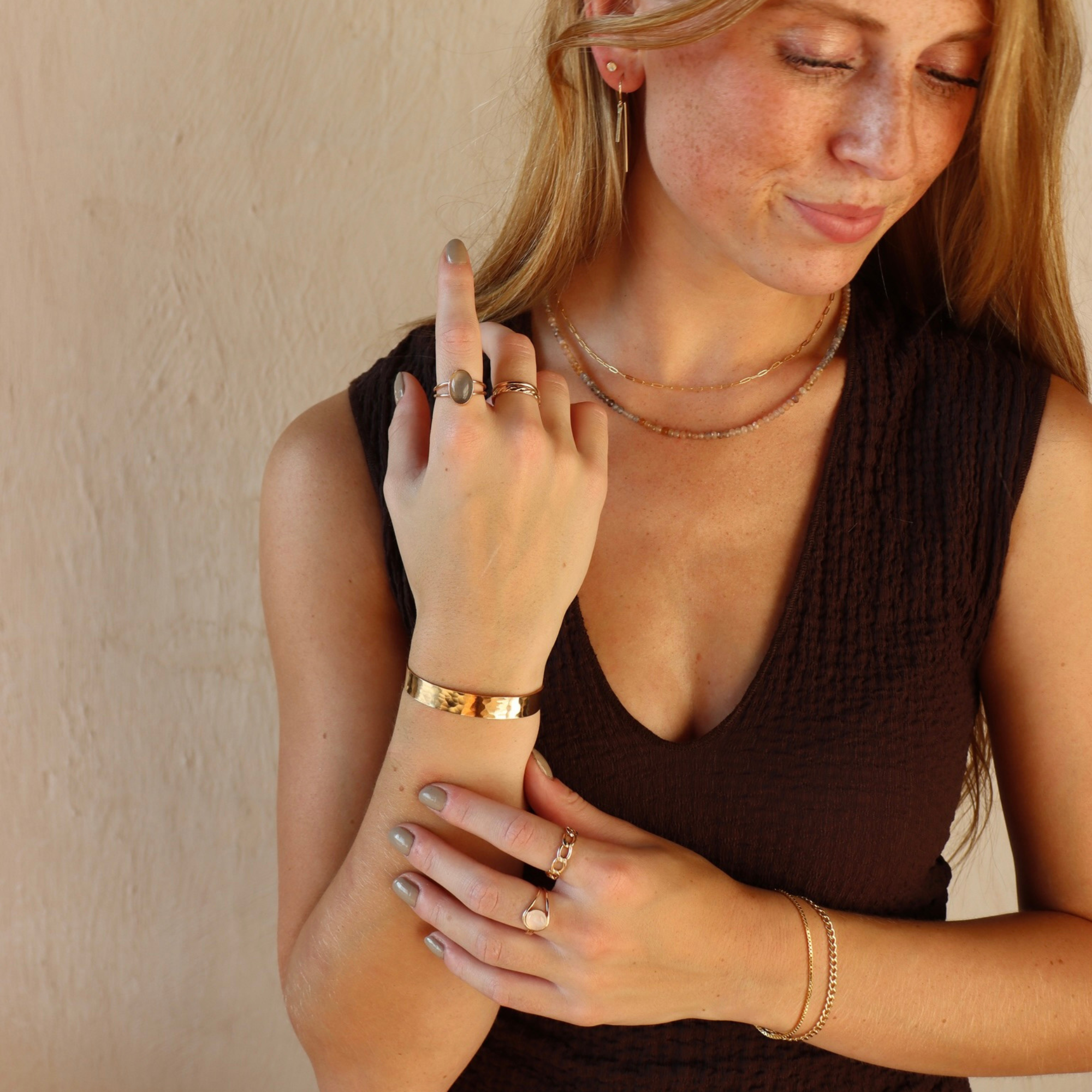 Model wearing the 14k Gold Fill Mirage Cuff, a polished hammered gold cuff bracelet, styled with gold rings, necklaces, and earrings in warm natural light.
