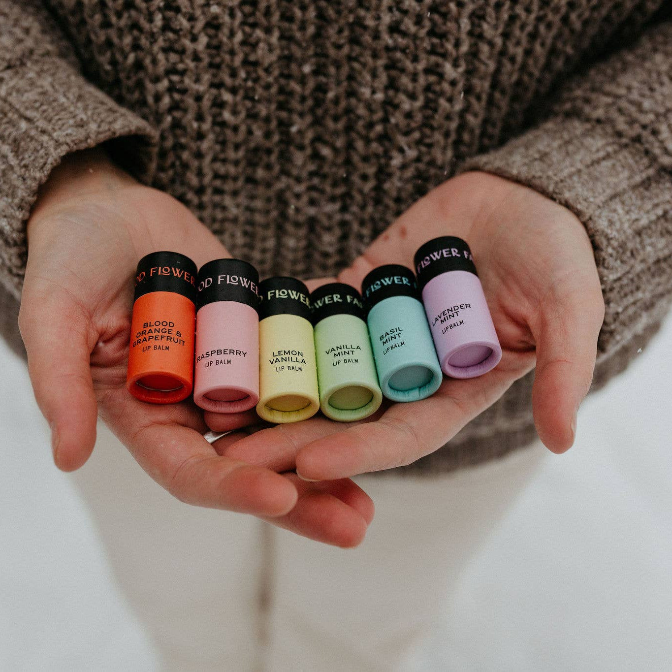 Person holding small  rainbow lip balms with labels in their hands.