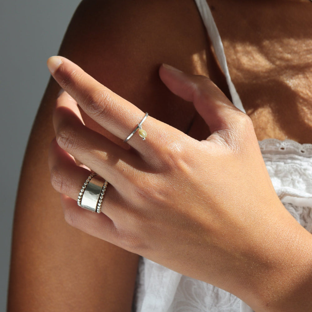 Model wearing a sterling silver hammered band with a kyanite gemstones freely hanging from the band. 