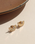 14k gold fill hammered metal ear jackets in a half moon shape, paired with April birthstone studs, displayed on a cream backdrop in the sunlight 
