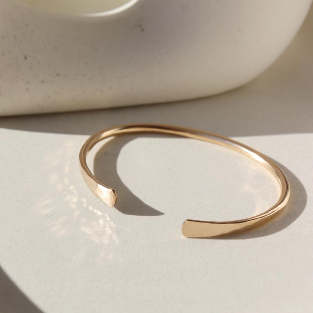 14k gold fill hammered cuff placed on a white plate sitting in the sunlight.