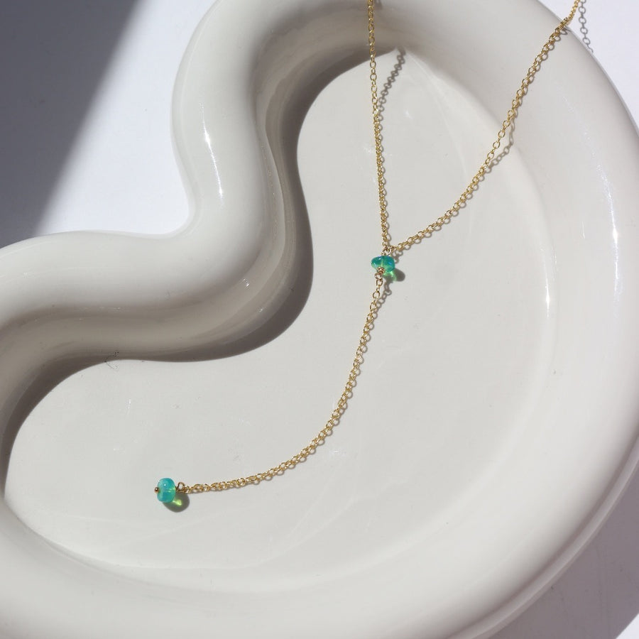 14k gold fill Green Opal Lariat Necklace laid on a white jewelry plate in the sunlight. This necklace features our simple chain connected by the Green opal gemstone dangling on the lariat is another green opal lariat.