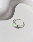 925 Sterling silver Sunset ring laid on a white paper on a white jewelry plate. This Ring features a simple hammered band with a 8mm Opal.