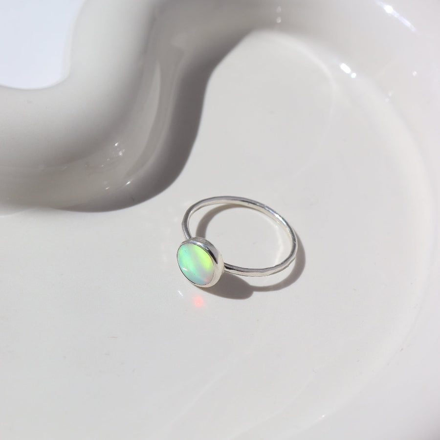 925 Sterling silver Sunset ring laid on a white paper on a white jewelry plate. This Ring features a simple hammered band with a 8mm Opal.