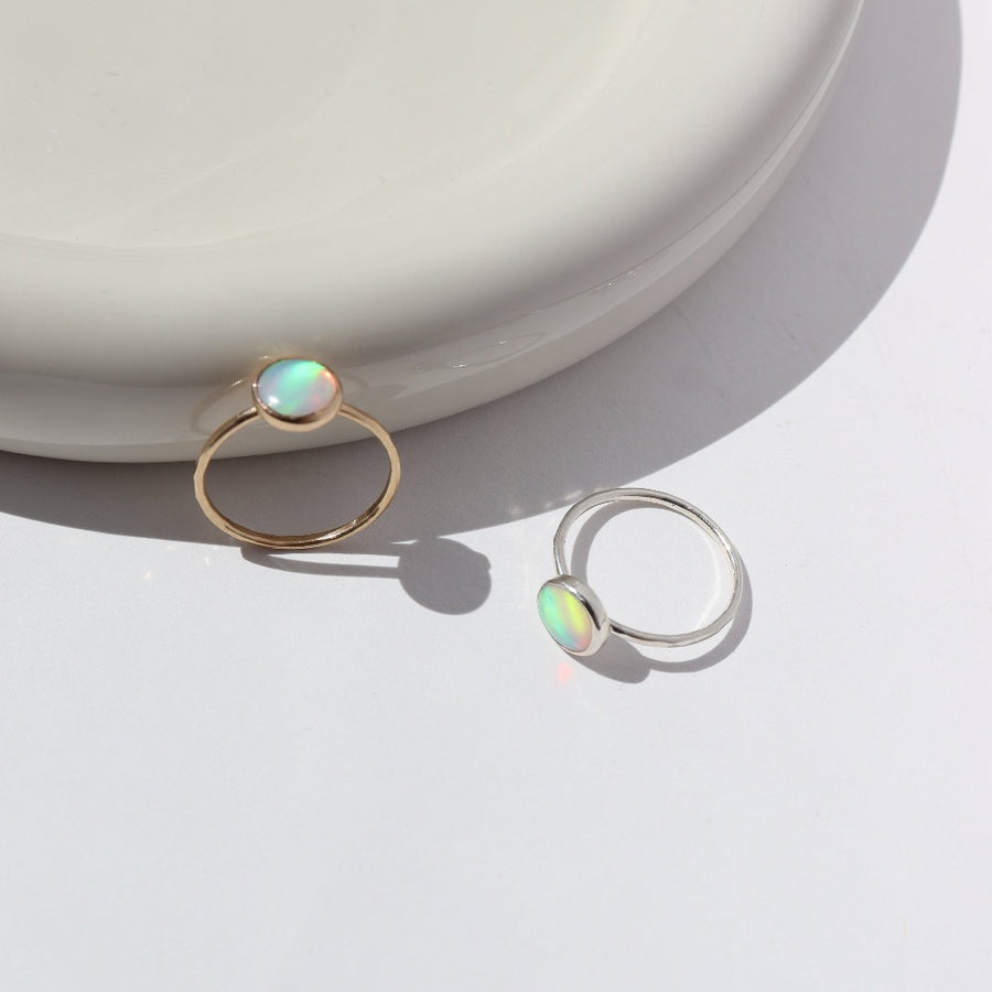 14k gold fill and 925 Sterling silver Sunset ring laid on a white paper on a white jewelry plate. This Ring features a simple hammered band with a 8mm Opal.
