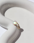14k gold fill Sunset ring laid on a white paper on a white jewelry plate. This Ring features a simple hammered band with a 8mm Opal.