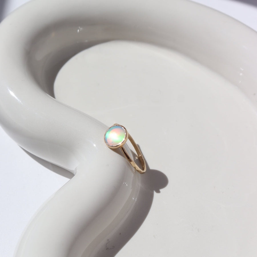 14k gold fill Sunset ring laid on a white paper on a white jewelry plate. This Ring features a simple hammered band with a 8mm Opal.