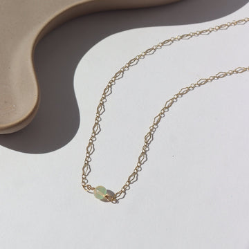 14k gold fill Frankie Opal Necklace laid on a white plate in the sunlight. This Necklace features our Clara chain with the Opal ball bead. 