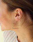 handmade 14k gold fill slide earrings in a heart shape, photographed on a smiling model