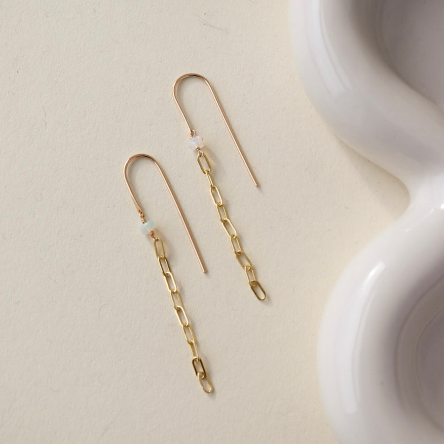gold chain earrings featuring a small pearl on a hook-style earring, photographed on a sunlit table