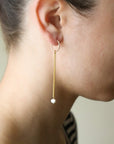 delicate chain hanging from a small hoop earring, with a small pearl at the end, photographed on a model