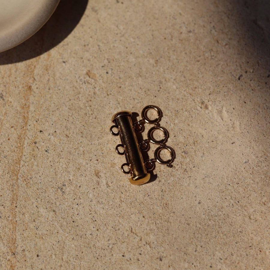 14k gold fill Necklace layering clasp laid on a stone plate in the sunlight.