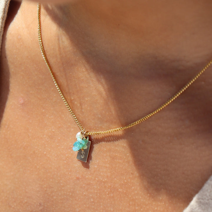 14k gold fill chain necklace featuring an initial stamped tag, three blue opal chips, and a  pearl charm, photographed on a model wearing a white top