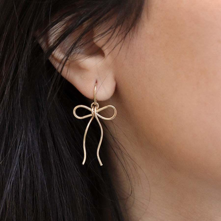 delicate gold fill bow earring hand made by Token Jewelry, photographed on a model