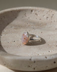 a sterling silver hand-set ocean jasper ring laid out on a cream colored backdrop in the sun