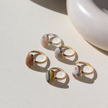 14k gold fill and sterling silver hand-set ocean jasper rings laid out on a cream colored backdrop in the sun
