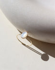 mother of pearl stone set in a bezel on a 14k gold fill skinny ring band, photographed on a table next to a white ceramic dish in the sun