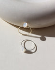 mother of pearl stone set in a bezel on a 14k gold fill skinny ring band, and a 925 sterling silver version, photographed on a table next to a white ceramic dish in the sun