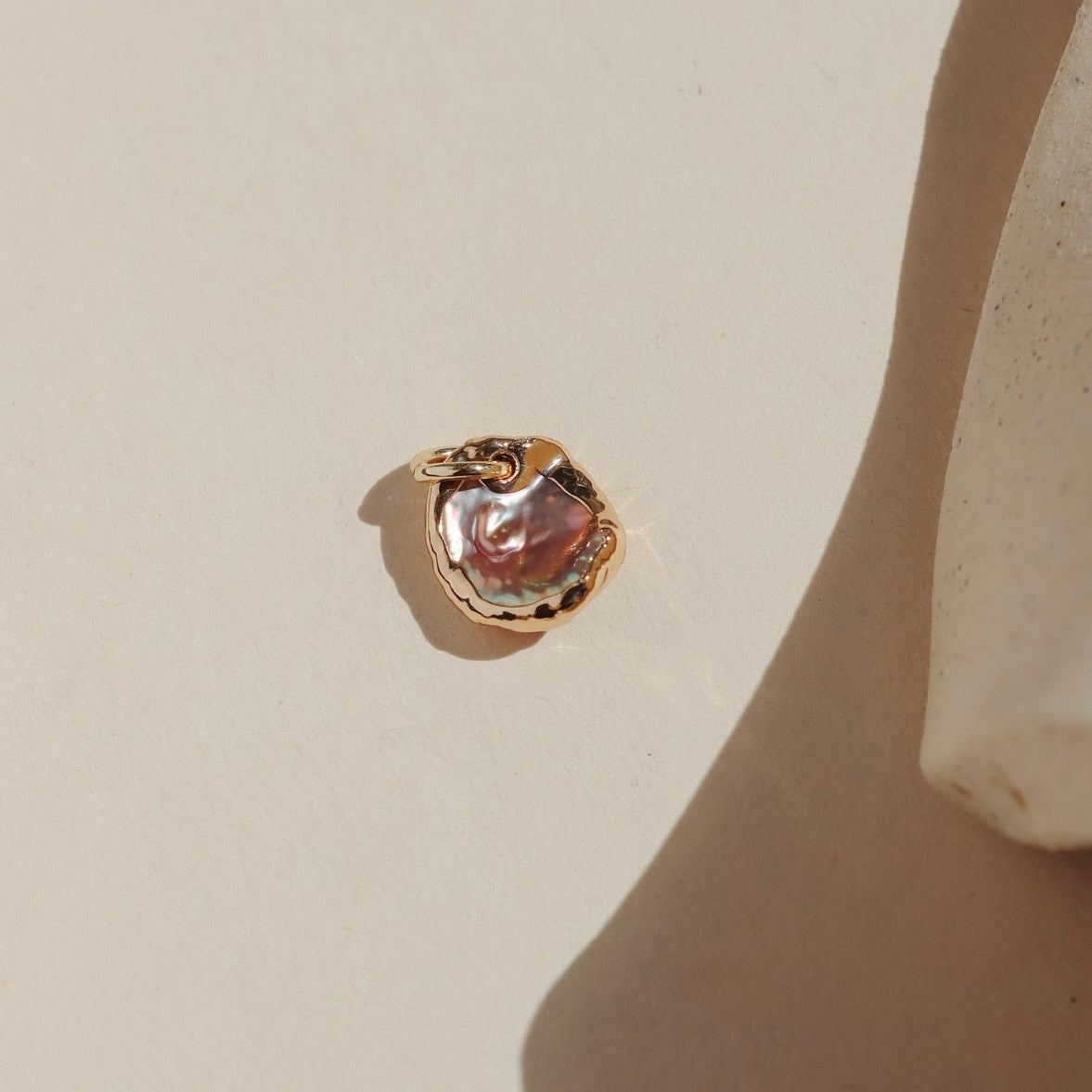 Organic keshi pearl charm with gold foil edging photographed in warm natural light.