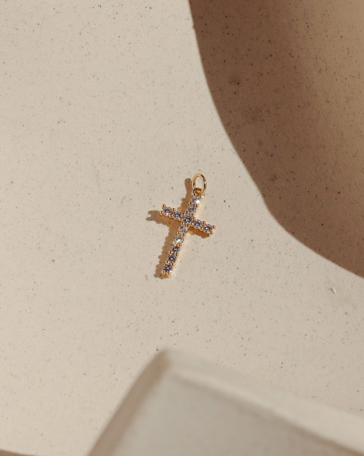 Gold cross charm set with sparkling pavé stones on a neutral background.