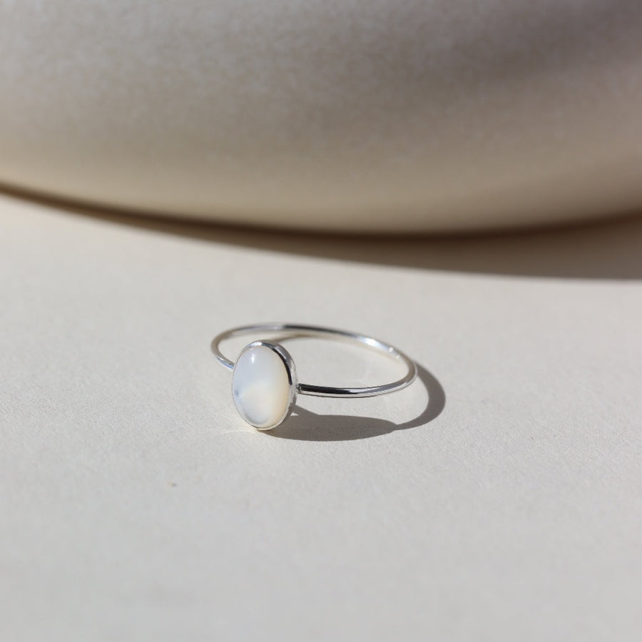 mother of pearl stone set in a bezel on a 925 sterling silver skinny ring band, photographed on a table next to a white ceramic dish in the sun