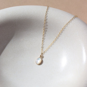 mother of pearl bezel pendant on a 14k gold fill delicate chain, photographed on a white ceramic dish