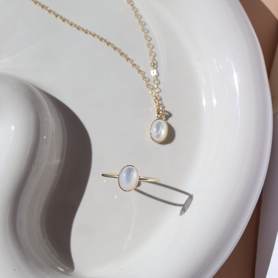 mother of pearl bezel pendant on a 14k gold fill delicate chain, and a mother of pearl ring,  photographed on a white ceramic dish