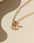 14k gold fill monogram toggle necklace laid on a tan paper in the sunlight. This necklace features the narrow link chain connected by a toggle with the monogram disc. 