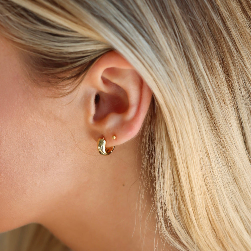 Close-up of a person wearing a gold hoop earring with blonde hair.