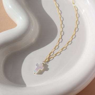 a mother of pearl white cross pendant on a 14k gold fill chain, lying on a white ceramic dish