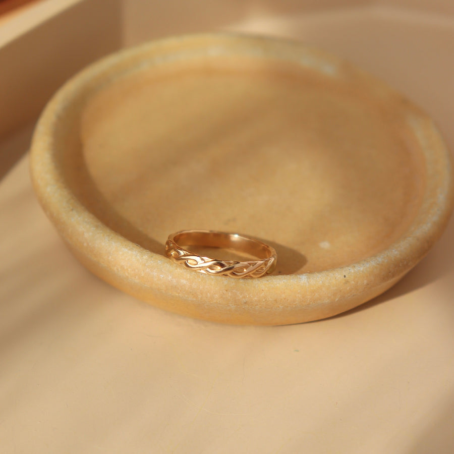 14k gold fill Helix run placed on a peach plate in the sunlight. This ring feature a small twist like band.