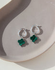 small sterling silver hoop earrings featuring a dangling clover shaped malachite stone, photographed on a sunny ceramic dish