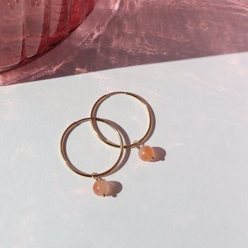 14k gold fill Cherry Blossom Hoops laid on a white plate in the sunlight. These earring feature a simple hoop earring with the perfect mini gemstone dangle. The gemstone featured in this earring is a Cherry Agate Sphere.
