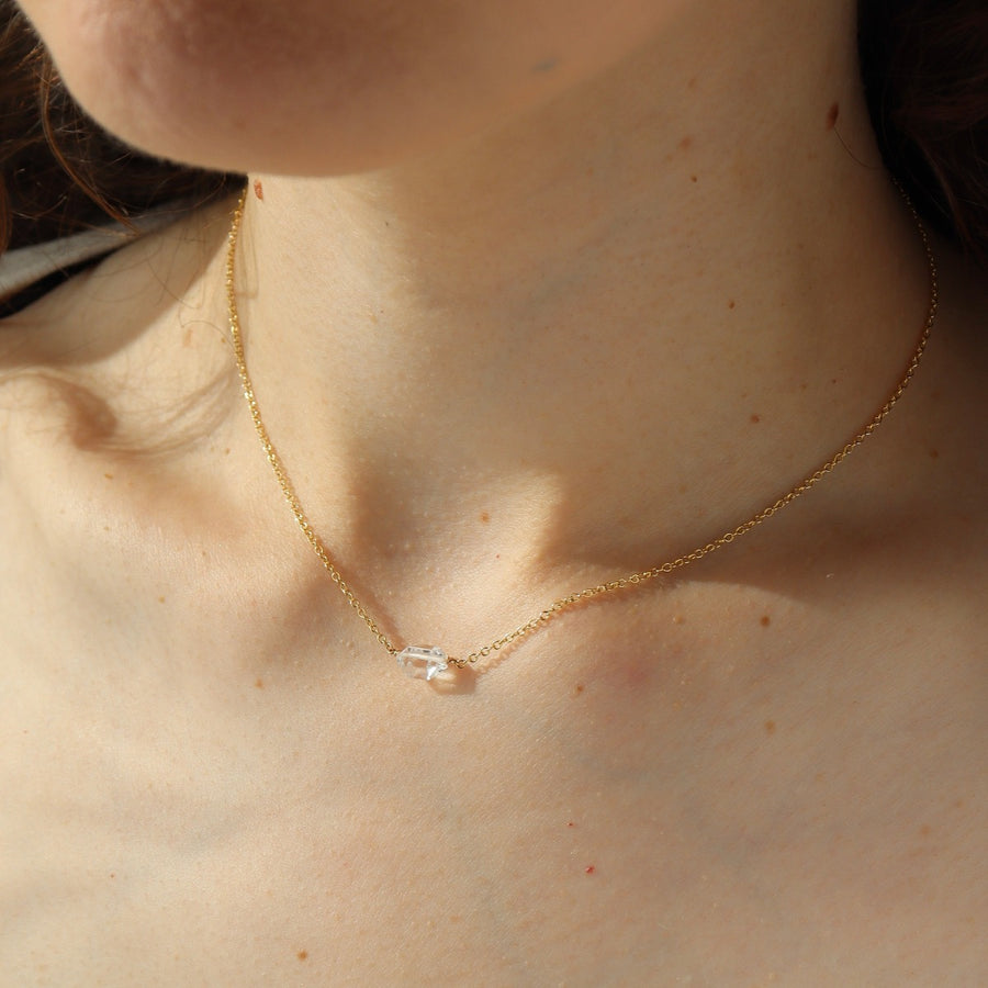 a clear double terminated quartz gemstone, known as a Herkimer Diamond, hangs from a delicate gold filled oval cable chain and is displayed on a ceramic jewelry dish